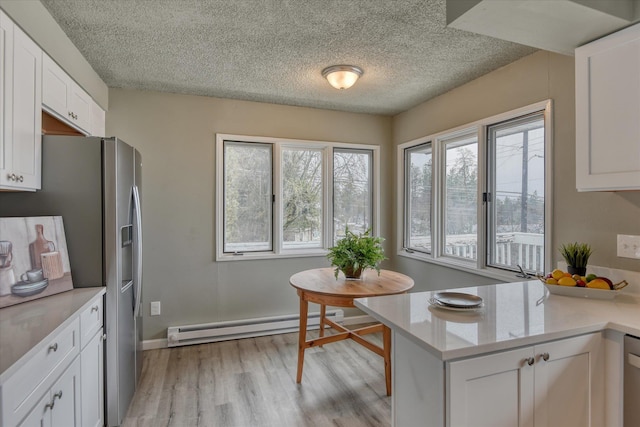 kitchen with stainless steel appliances, baseboard heating, white cabinetry, light stone countertops, and light wood-type flooring