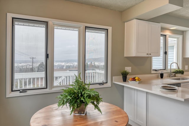 kitchen featuring light countertops, white cabinets, a sink, a textured ceiling, and a peninsula