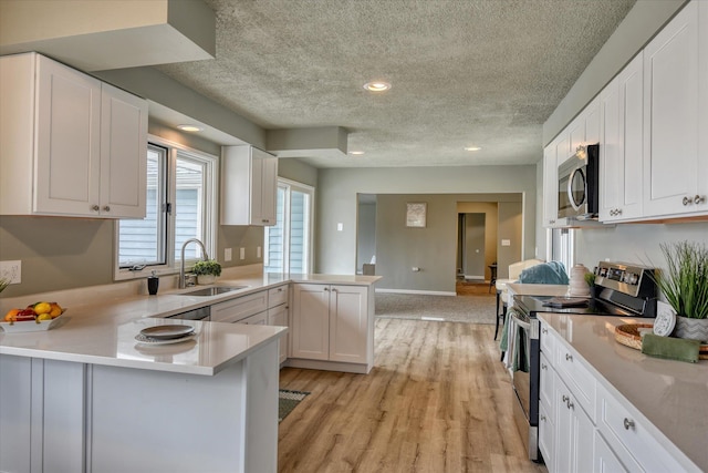 kitchen featuring stainless steel appliances, light countertops, white cabinetry, a sink, and a peninsula