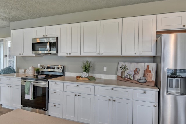 kitchen with a textured ceiling, appliances with stainless steel finishes, white cabinets, and light countertops