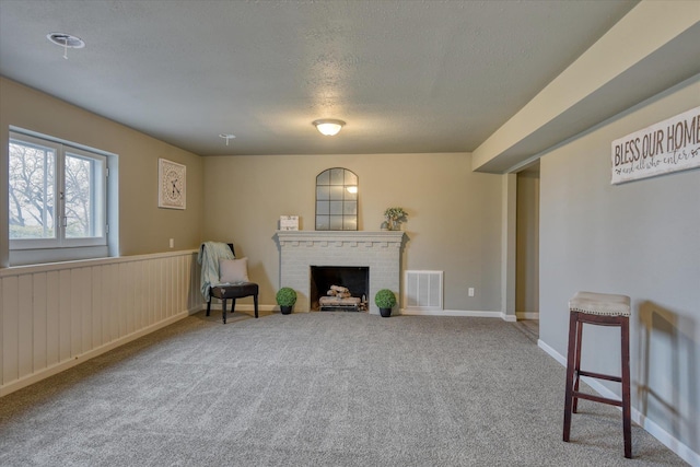 sitting room featuring a textured ceiling, a wainscoted wall, carpet flooring, visible vents, and a brick fireplace