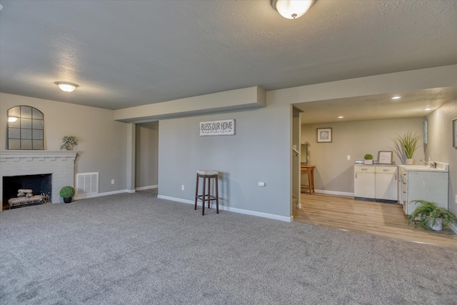 living area with light colored carpet, a fireplace, visible vents, and a textured ceiling