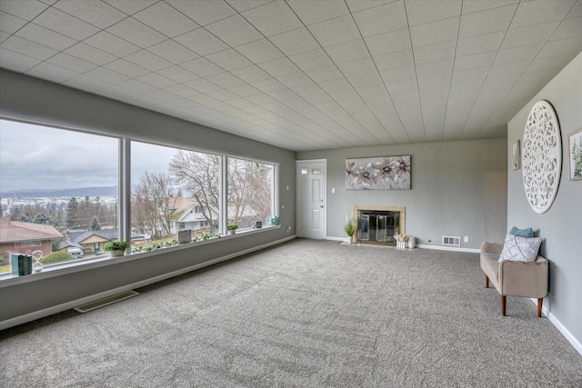 unfurnished living room featuring carpet floors, baseboards, visible vents, and a glass covered fireplace