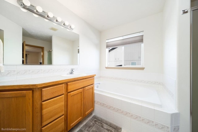 bathroom featuring a relaxing tiled tub and vanity