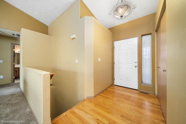 hall featuring lofted ceiling, light hardwood / wood-style floors, and a textured ceiling