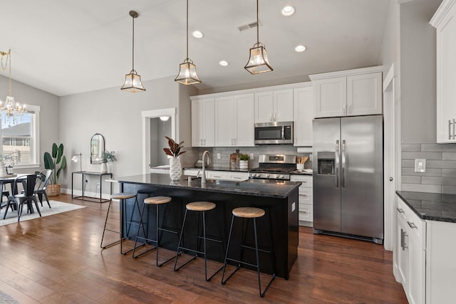 kitchen with hanging light fixtures, stainless steel appliances, an island with sink, and white cabinets