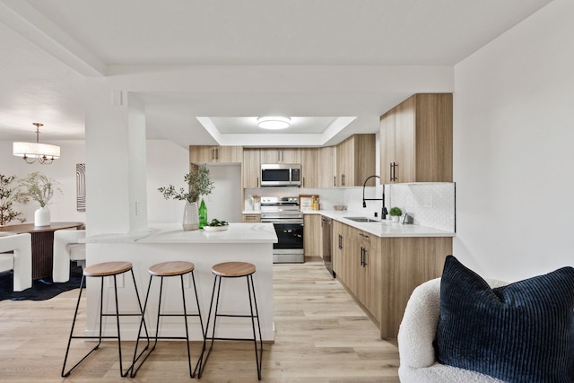 kitchen featuring sink, hanging light fixtures, a tray ceiling, kitchen peninsula, and stainless steel appliances