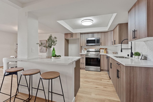 kitchen with tasteful backsplash, appliances with stainless steel finishes, sink, and light wood-type flooring