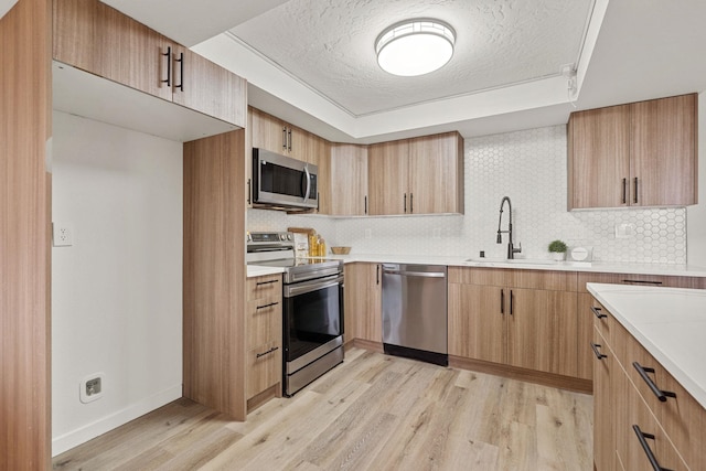 kitchen featuring sink, backsplash, stainless steel appliances, light hardwood / wood-style floors, and a textured ceiling