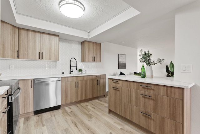 kitchen with tasteful backsplash, appliances with stainless steel finishes, a tray ceiling, and light wood-type flooring