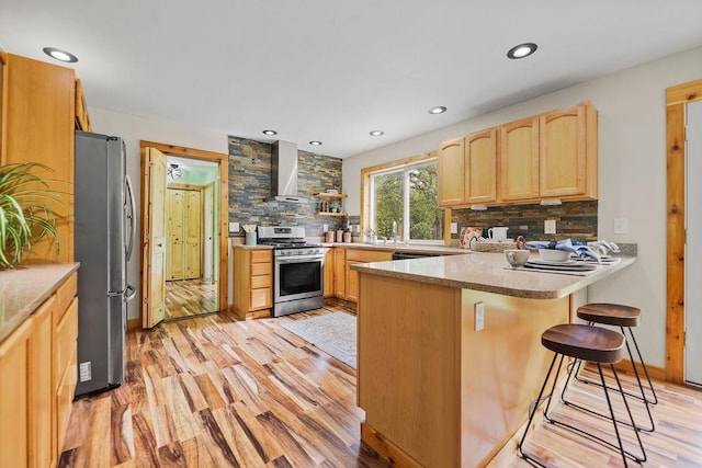 kitchen featuring wall chimney range hood, a breakfast bar, appliances with stainless steel finishes, light hardwood / wood-style floors, and kitchen peninsula