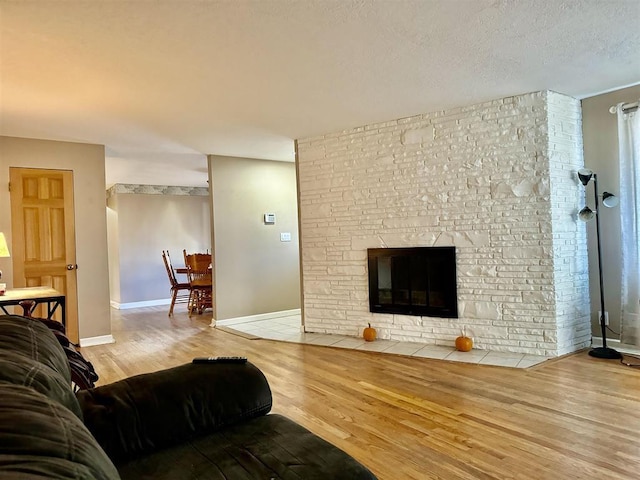 living room with a stone fireplace, a textured ceiling, and light hardwood / wood-style floors