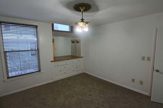 spare room with an inviting chandelier and dark colored carpet