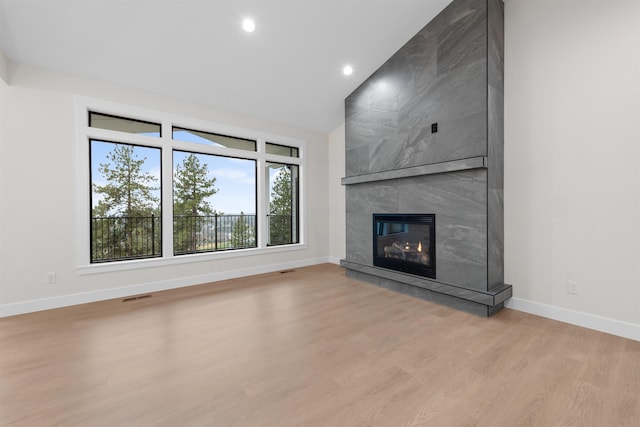 unfurnished living room with a premium fireplace, lofted ceiling, and light hardwood / wood-style floors