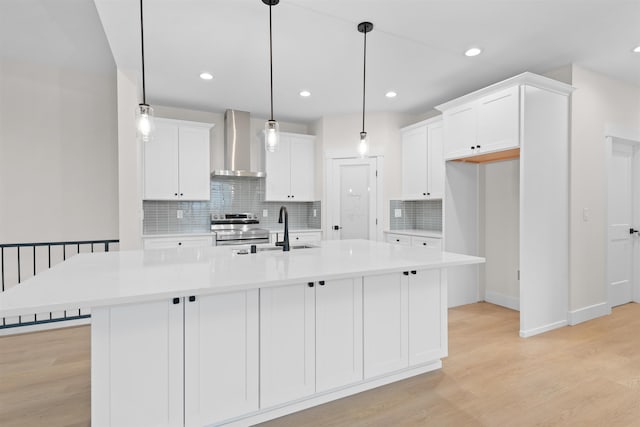 kitchen featuring wall chimney exhaust hood, sink, hanging light fixtures, a center island with sink, and electric stove