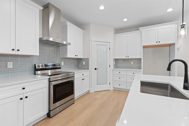 kitchen with white cabinetry, wall chimney range hood, stainless steel range with electric cooktop, and hanging light fixtures