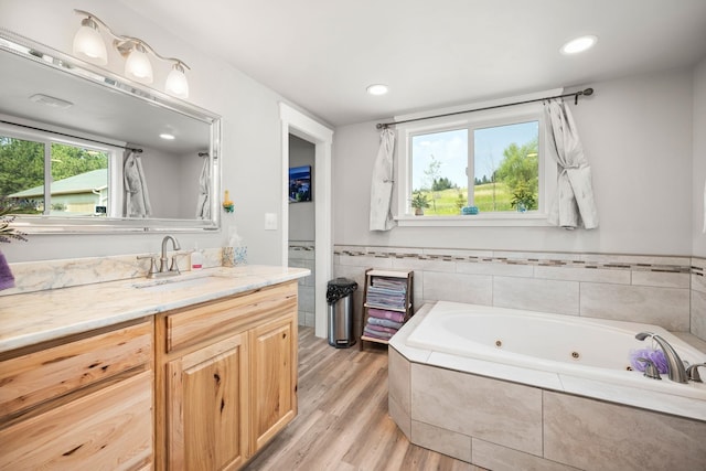 bathroom with a relaxing tiled tub, vanity, and hardwood / wood-style floors