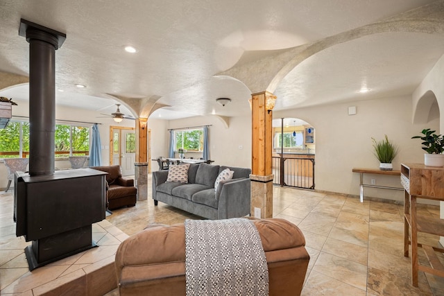 living room featuring ceiling fan, a wood stove, and a textured ceiling