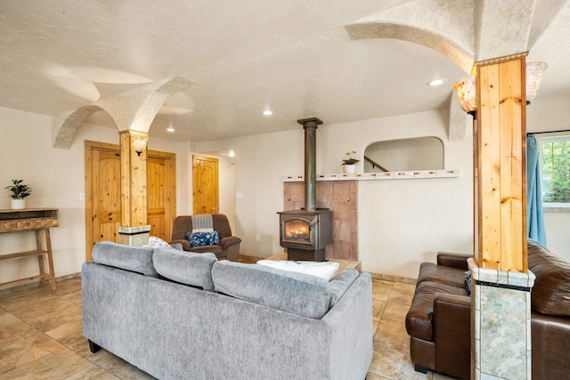 living room featuring decorative columns, a textured ceiling, and a wood stove