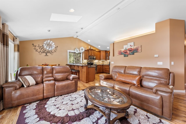 living room featuring an inviting chandelier, lofted ceiling with skylight, and light hardwood / wood-style floors