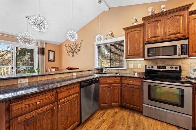 kitchen featuring appliances with stainless steel finishes, a wealth of natural light, sink, dark stone countertops, and hanging light fixtures