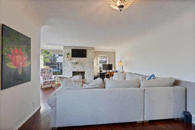 living room featuring dark wood-type flooring, a textured ceiling, and a fireplace