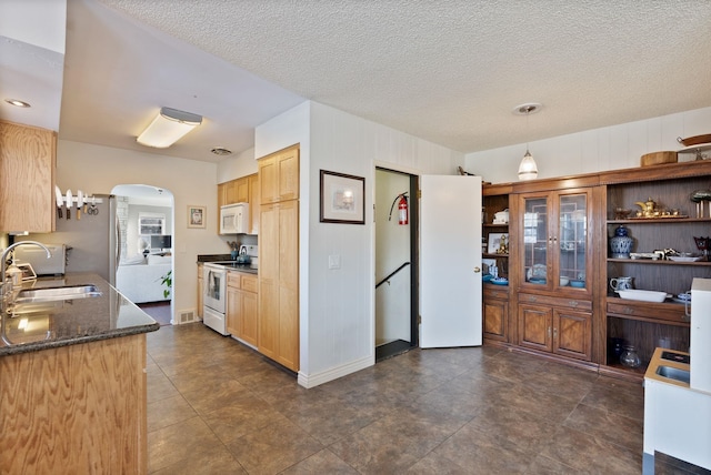 kitchen featuring sink, white appliances, dark stone countertops, a textured ceiling, and decorative light fixtures