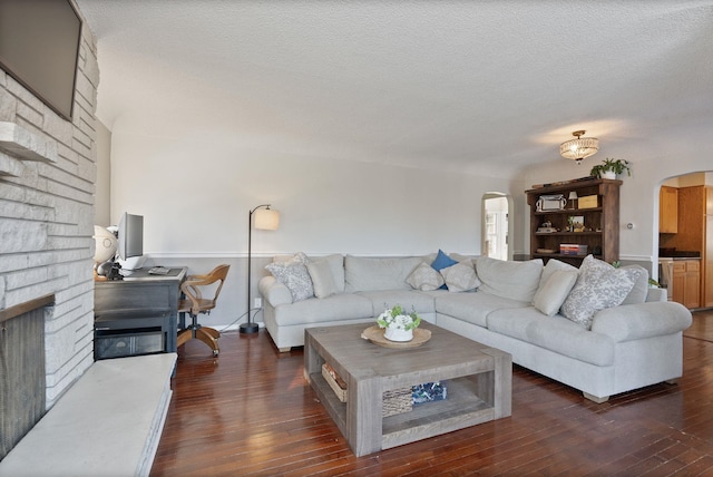 living room with dark wood-type flooring, a brick fireplace, and a textured ceiling