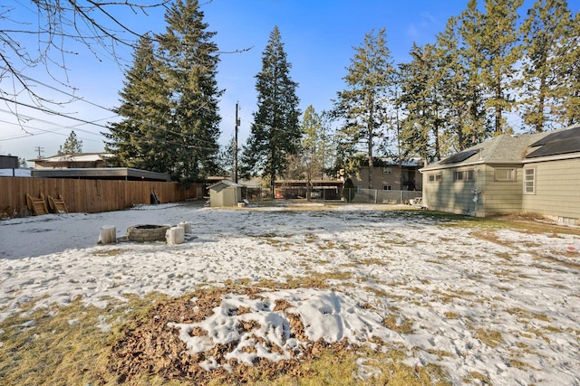 yard covered in snow featuring a storage shed and an outdoor fire pit