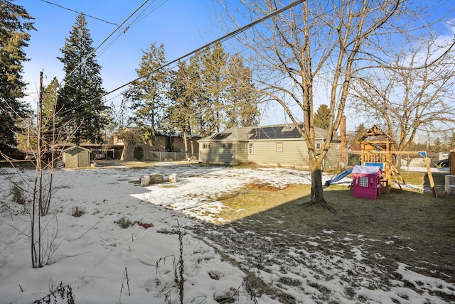 snowy yard featuring a playground and a storage unit