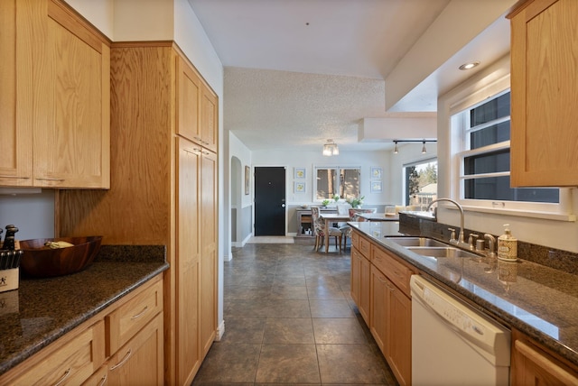 kitchen featuring sink, dishwasher, a textured ceiling, light brown cabinetry, and dark stone counters