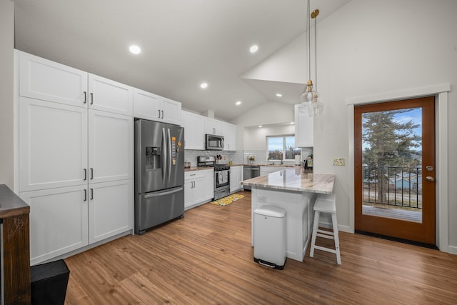 kitchen featuring a breakfast bar, hanging light fixtures, kitchen peninsula, stainless steel appliances, and white cabinets