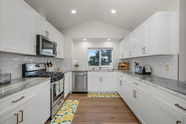 kitchen featuring light stone counters, lofted ceiling, appliances with stainless steel finishes, and white cabinets