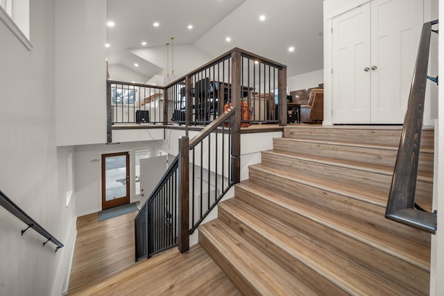 stairway with hardwood / wood-style flooring and high vaulted ceiling