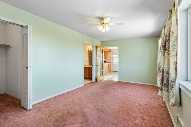 unfurnished bedroom featuring ensuite bathroom, a spacious closet, light colored carpet, a closet, and ceiling fan