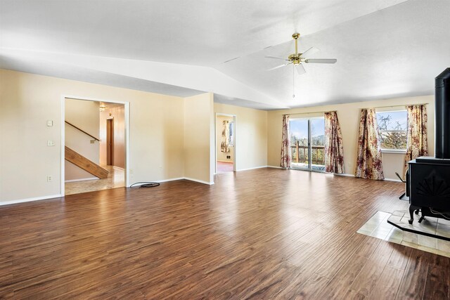 unfurnished living room with ceiling fan, dark hardwood / wood-style flooring, vaulted ceiling, and a wood stove