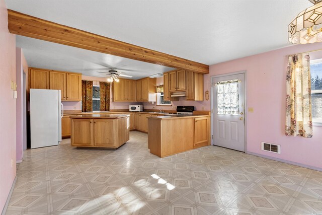 kitchen featuring pendant lighting, range, a center island, white refrigerator, and beamed ceiling