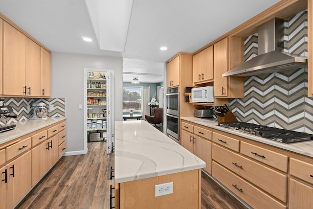 kitchen featuring light brown cabinetry, a center island, stainless steel appliances, dark wood-type flooring, and wall chimney range hood