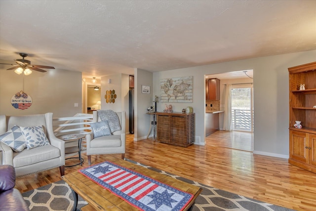 living room with ceiling fan, a textured ceiling, and light wood-type flooring