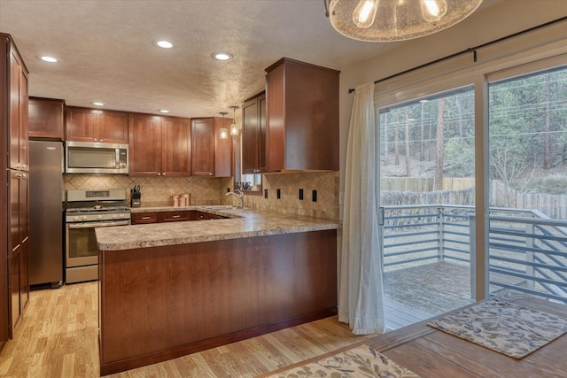 kitchen featuring stainless steel appliances, plenty of natural light, light wood-type flooring, and kitchen peninsula