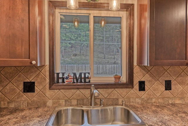 kitchen with sink, backsplash, light stone counters, and decorative light fixtures