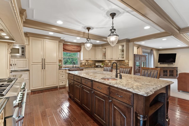 kitchen with sink, a center island with sink, dark brown cabinetry, and cream cabinetry