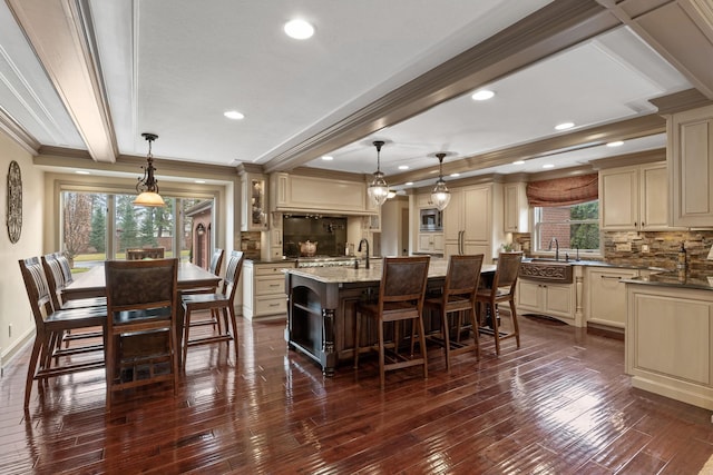 kitchen with hanging light fixtures, cream cabinets, and a kitchen island with sink