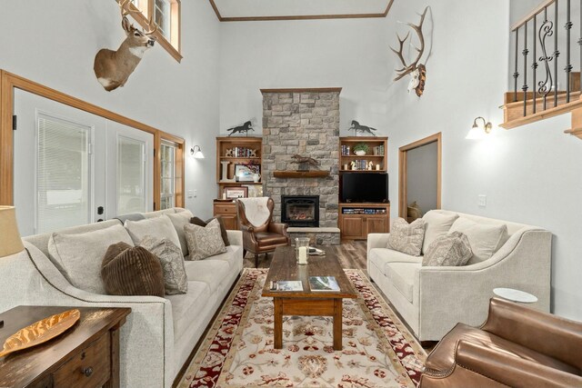 living room with crown molding, light hardwood / wood-style flooring, a towering ceiling, a stone fireplace, and french doors