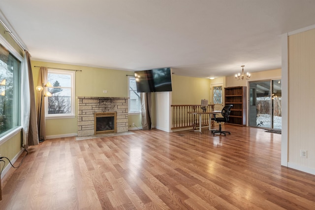 unfurnished living room with a stone fireplace, a chandelier, and light wood-type flooring