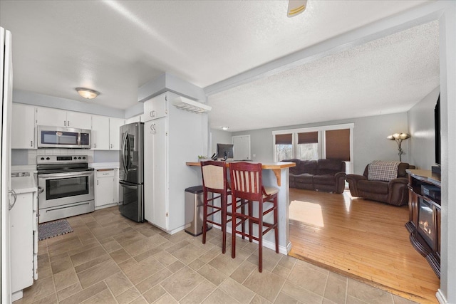 kitchen with stainless steel appliances, tasteful backsplash, white cabinets, and a textured ceiling