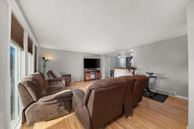 living room featuring ceiling fan, light hardwood / wood-style floors, and a textured ceiling