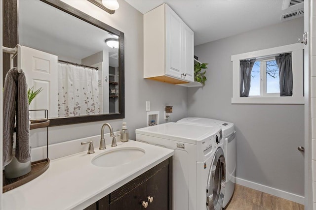 washroom with sink, light hardwood / wood-style flooring, washing machine and dryer, and cabinets