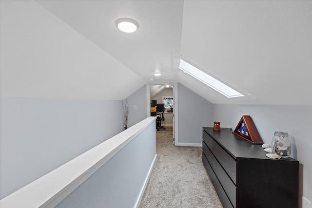 hallway with vaulted ceiling with skylight and light colored carpet