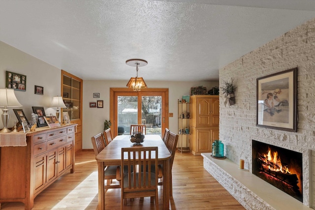 dining area featuring a fireplace, light hardwood / wood-style flooring, and a textured ceiling